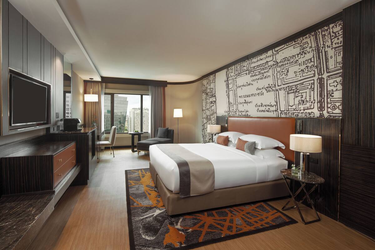 A modern hotel room with a large bed, a desk, a TV, and a city view.
