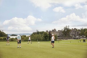 A golf course with players, a flag, and a castle in the background.