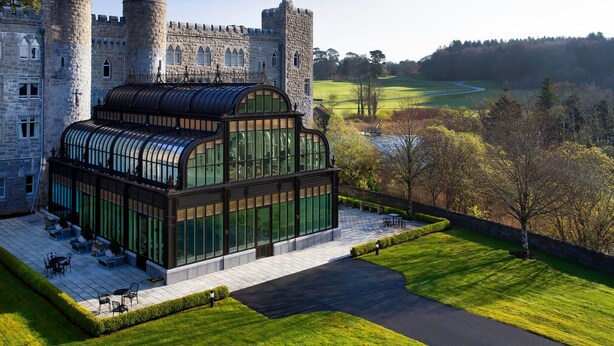Un château doté d’une véranda en verre, d’une pelouse et offrant une vue sur une rivière.