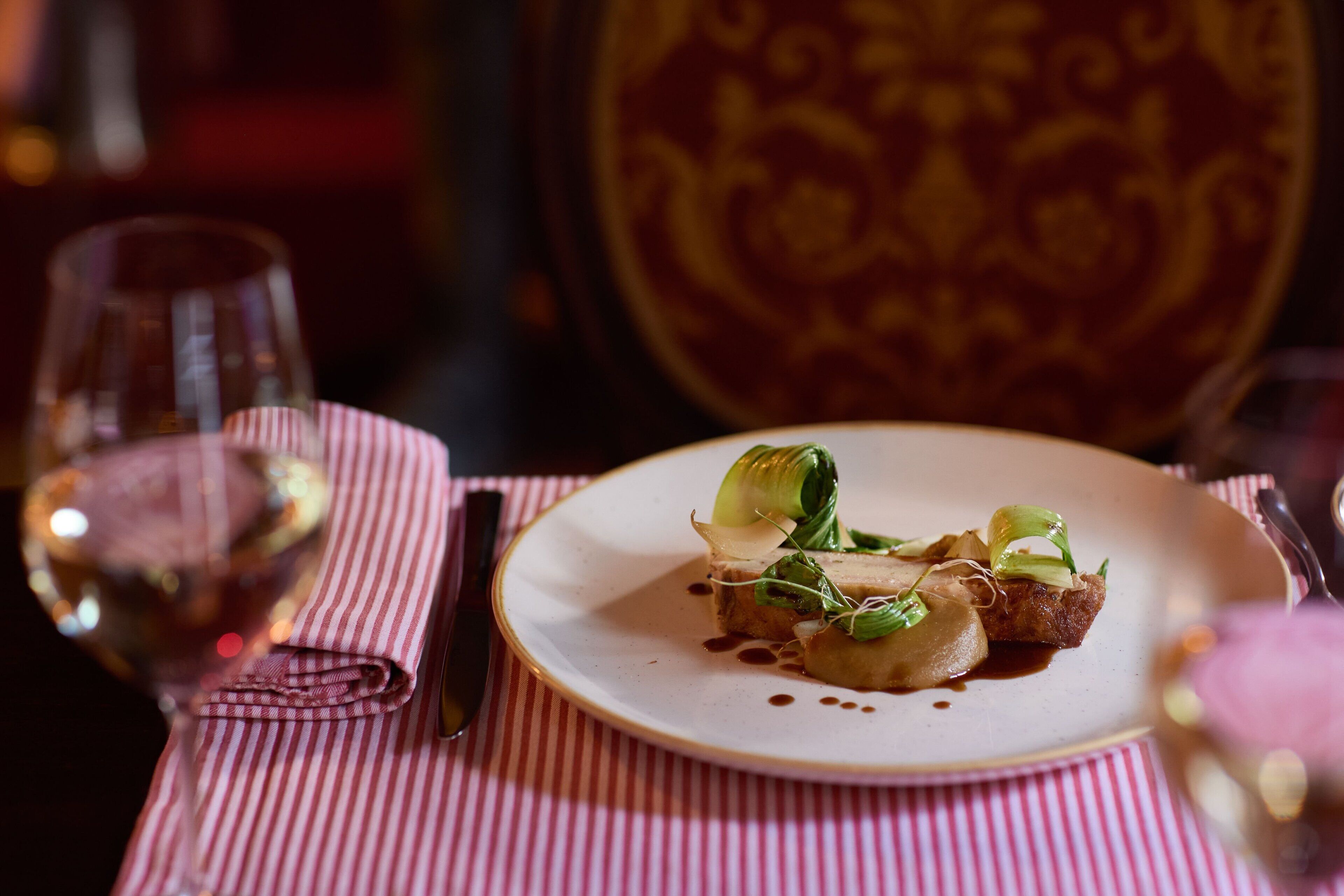 A dining table with a plate of food, a glass of wine, and a striped napkin.