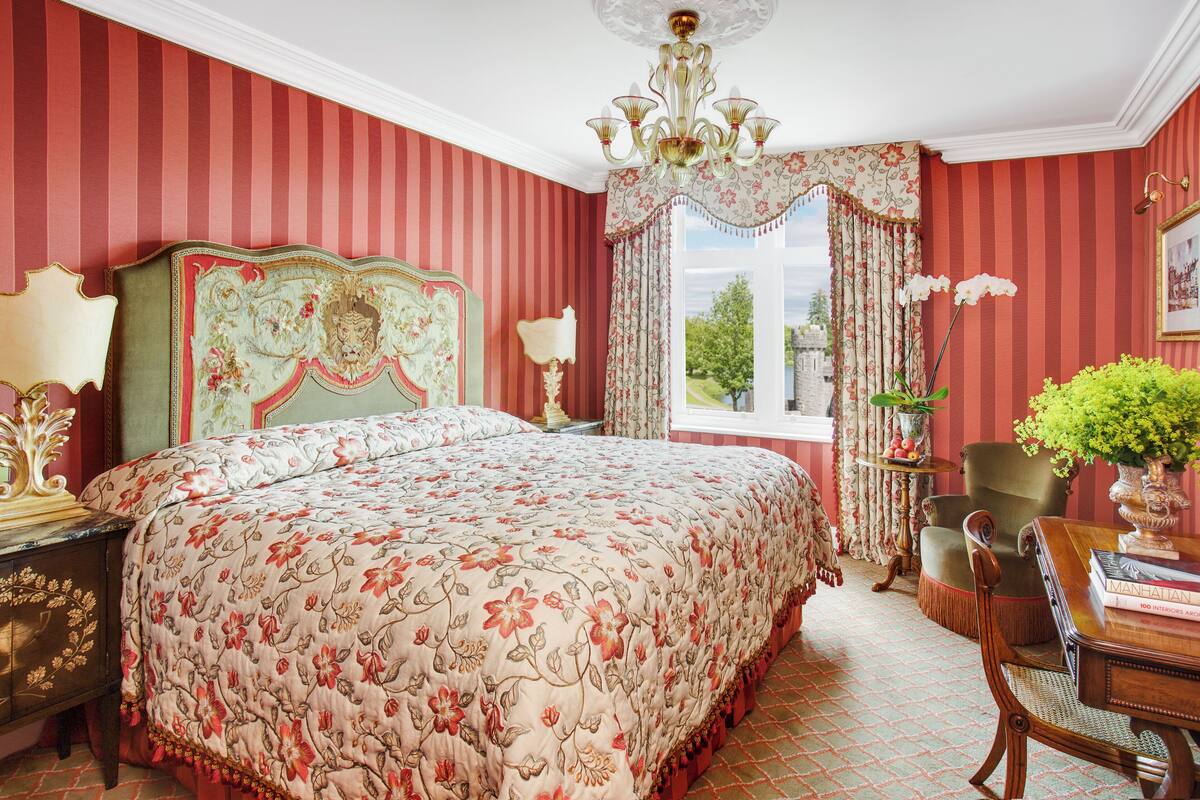 Una habitación con una cama grande, una araña, un escritorio con una silla y una ventana con cortinas.