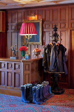 A room with wooden paneling, a red lamp, a coat rack with jackets, a statue, and a vase with red flowers.