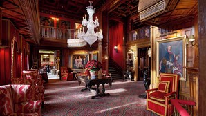 Un hall d’entrée somptueux, agrémenté d’un imposant lustre, d’un tapis rouge à motifs et de meubles richement décorés.