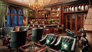 A grand room with leather armchairs, a chandelier, and a bar area with wooden cabinets.