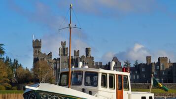 A green and white boat with a cabin, moving on water with a castle in the background.