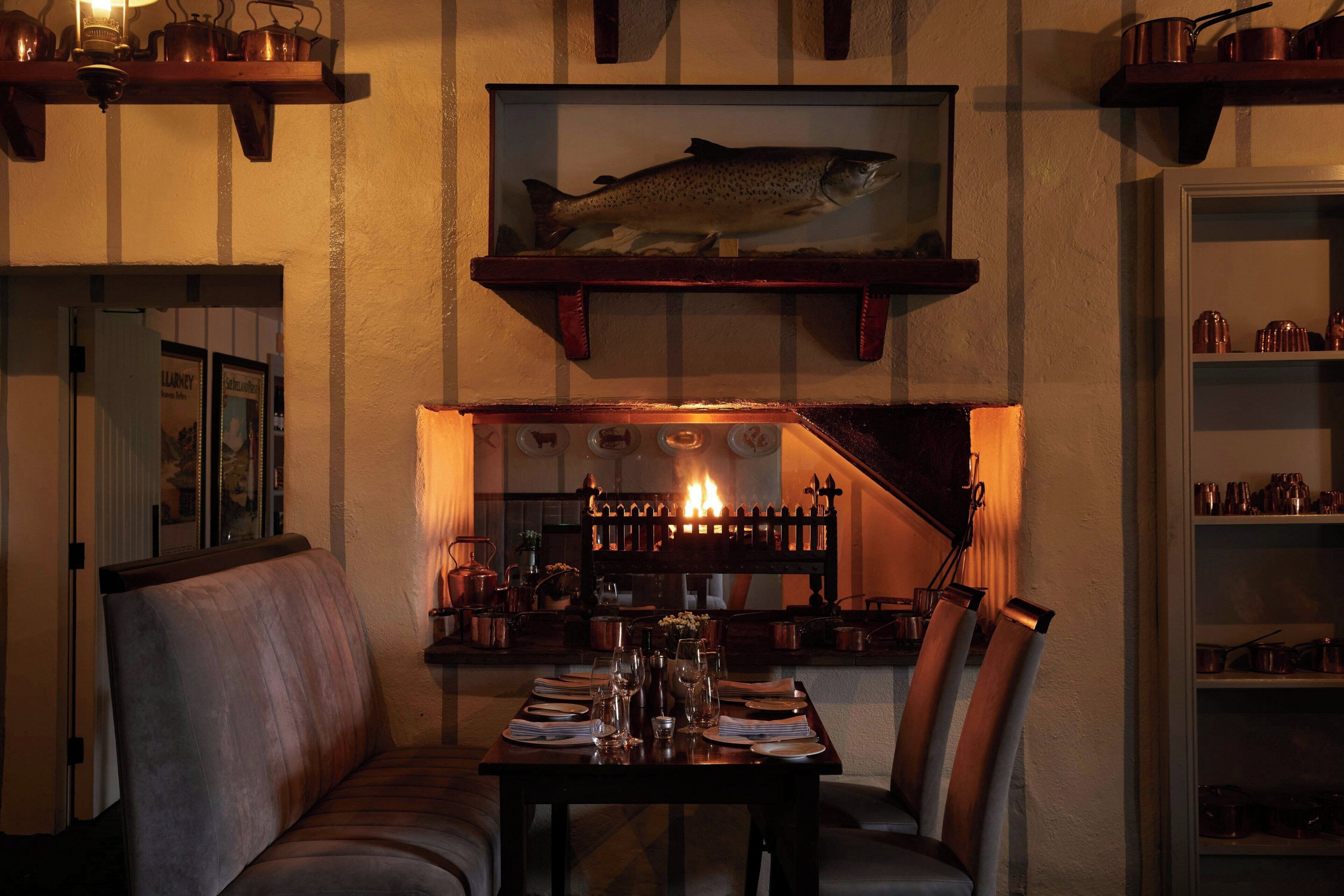 A dining area with a table set for two, a fireplace, and shelves with kitchenware.