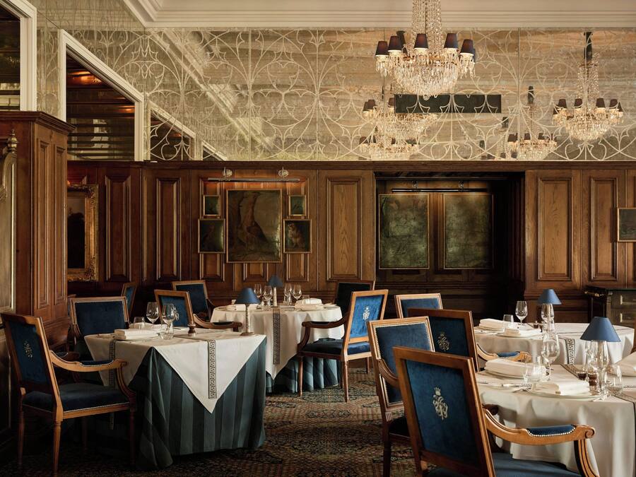 Un comedor formal con múltiples mesas, sillas, candelabros y paneles de madera.