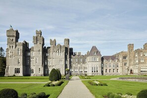 A large, historic castle with a central courtyard, multiple towers, and a well-maintained lawn.