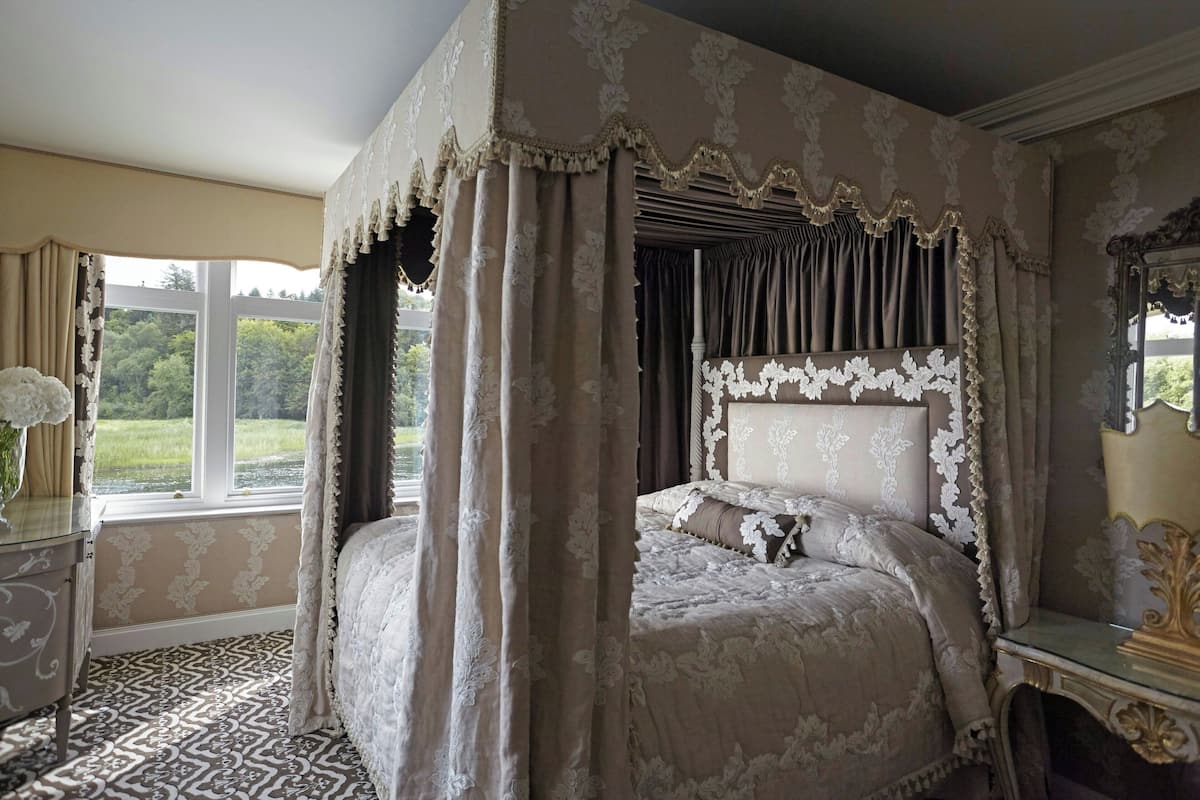 Un dormitorio con cama a dosel, un ventanal con cortinas, un espejo y suelo estampado.