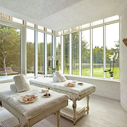 A spa room with two massage tables, large windows, and a view of the outdoors.