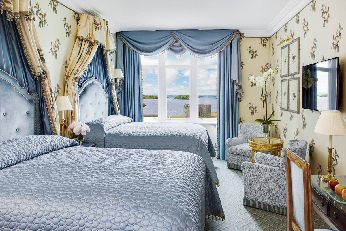 A hotel room with two beds, a sitting area, a television, and a view of the water.