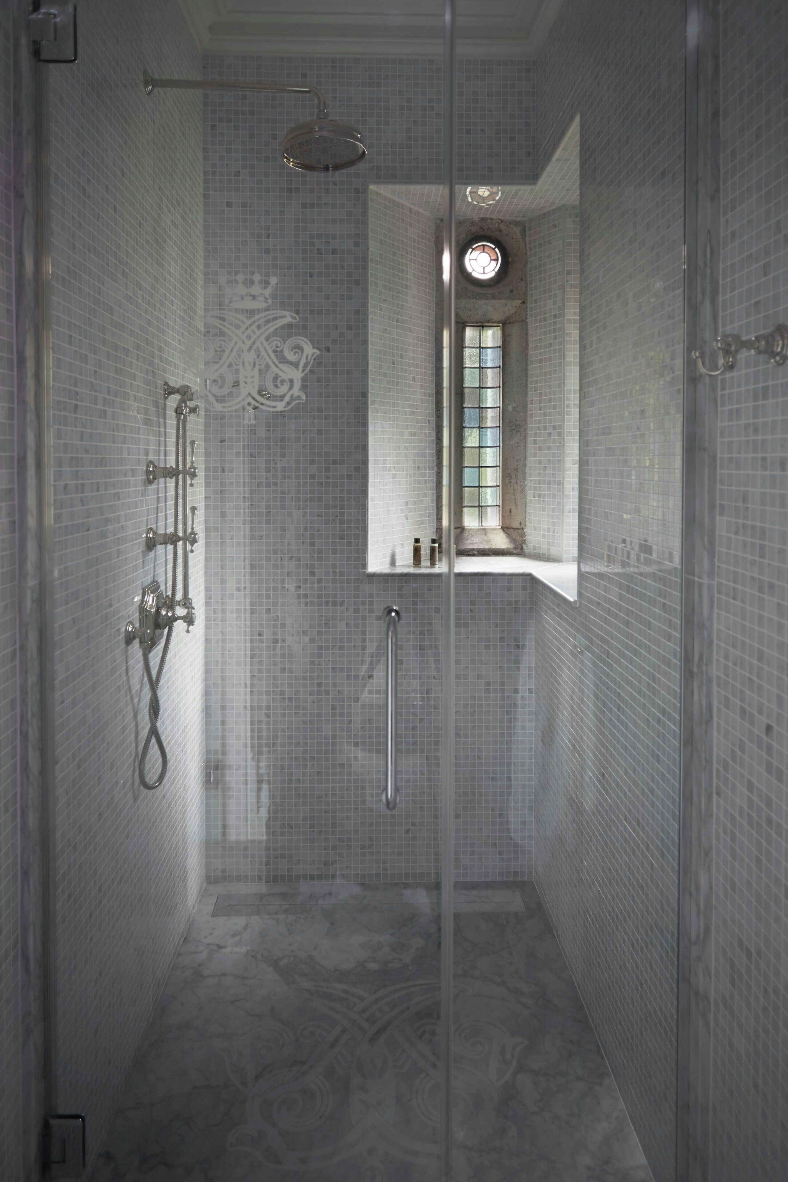 A narrow, tiled shower with a glass door, a visible window, and a decorative crown motif on the wall.