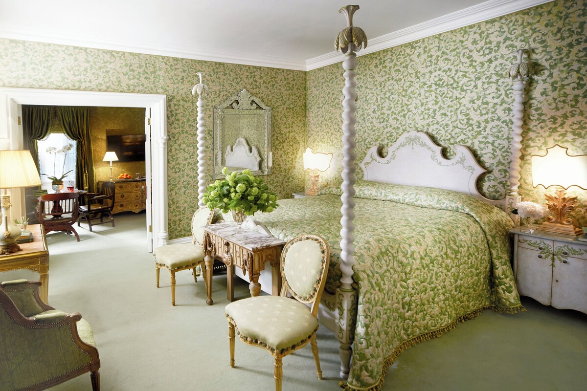 A bedroom with a four-poster bed, a sitting area with a table and chairs, and a dresser.