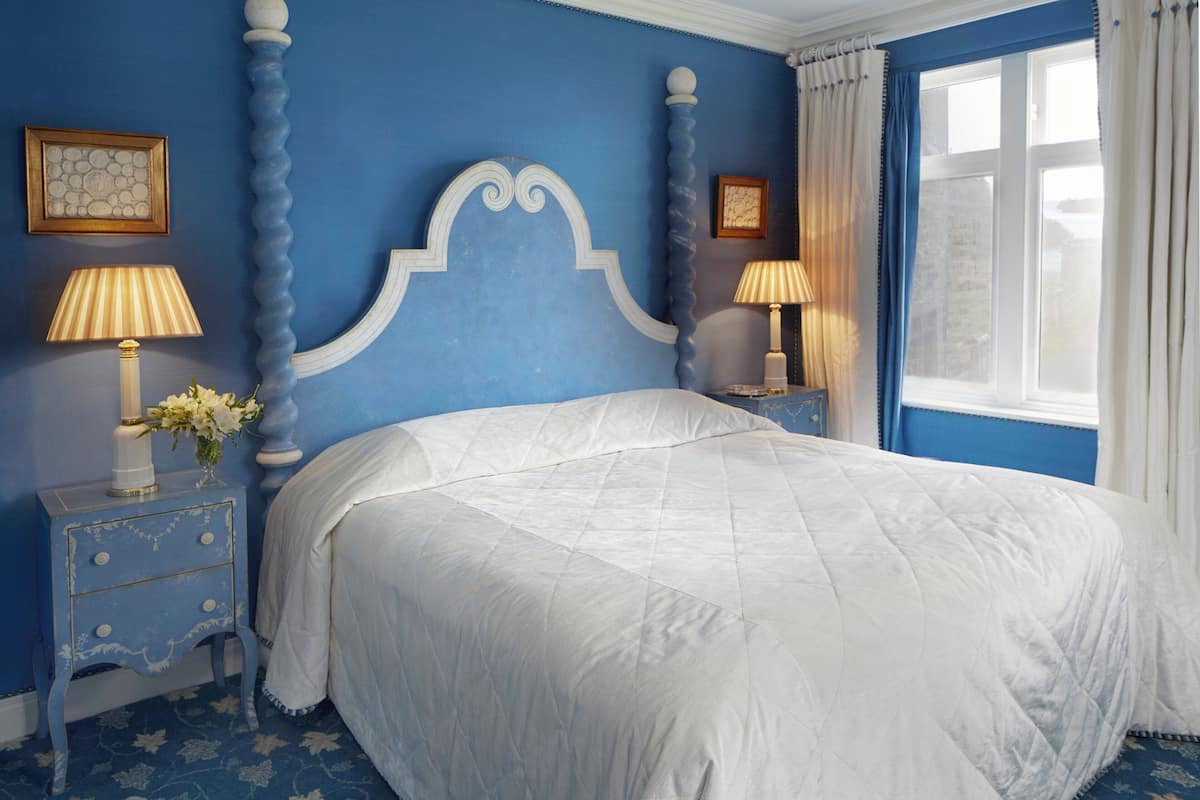 Un dormitorio con una cama grande, dos mesitas de noche con lámparas y un ventanal con cortinas.