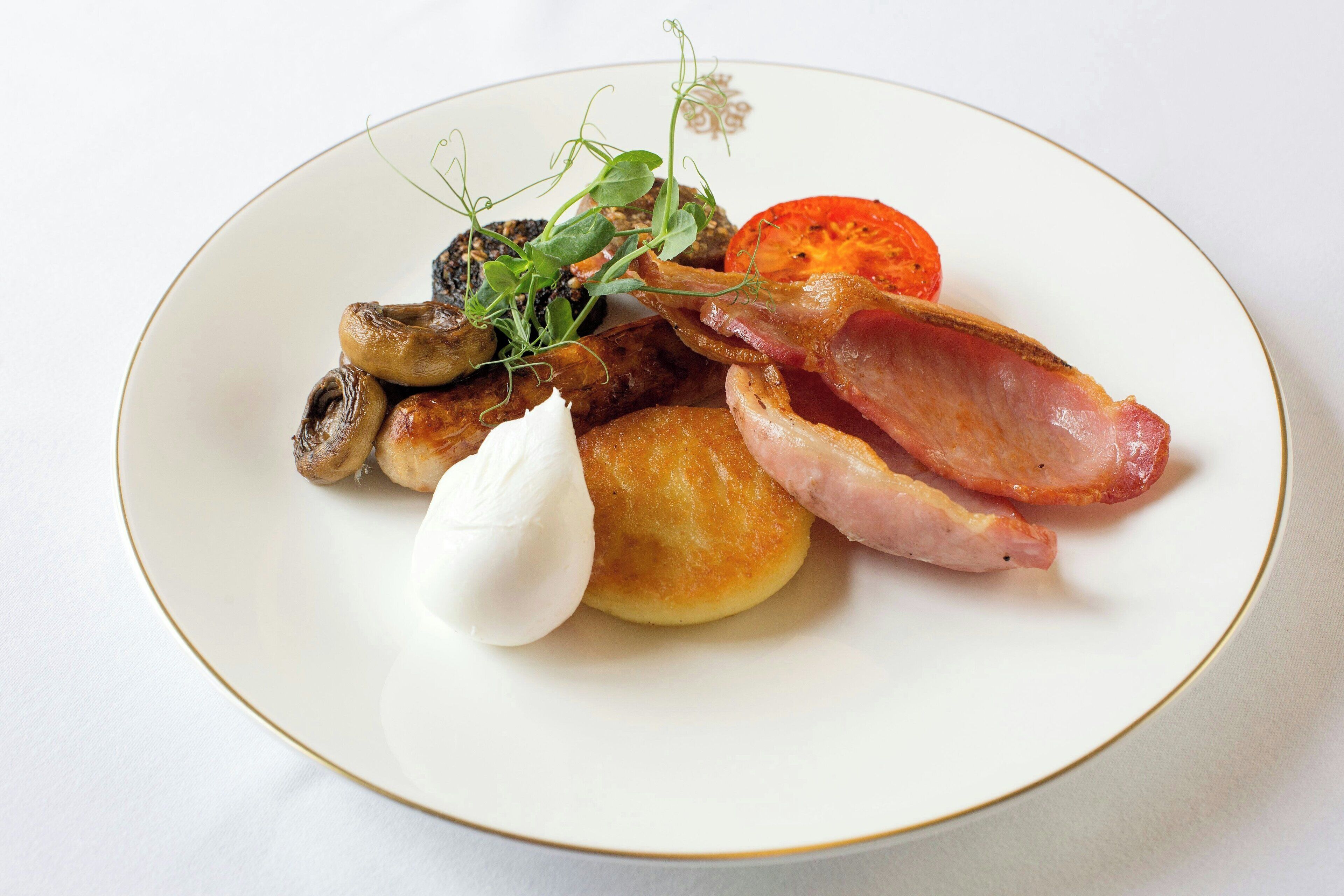 A plate with various food items including mushrooms, bacon, a tomato slice, and a dollop of cream.