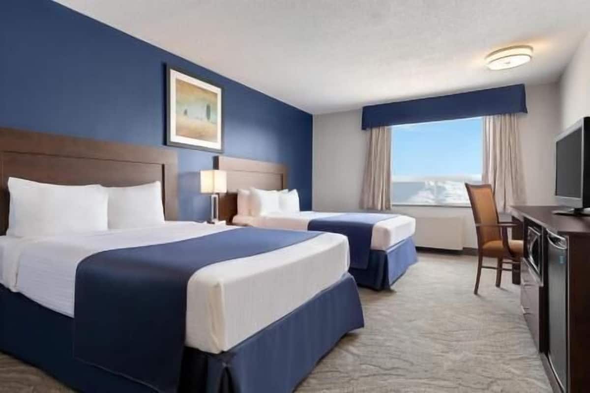 A hotel room with two beds, a desk, a chair, a television, and a window with a view.