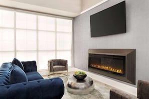 A modern living room with a large sofa, a fireplace, and a flat-screen TV mounted on the wall. - Travelodge by Wyndham Timmins (Timmins)