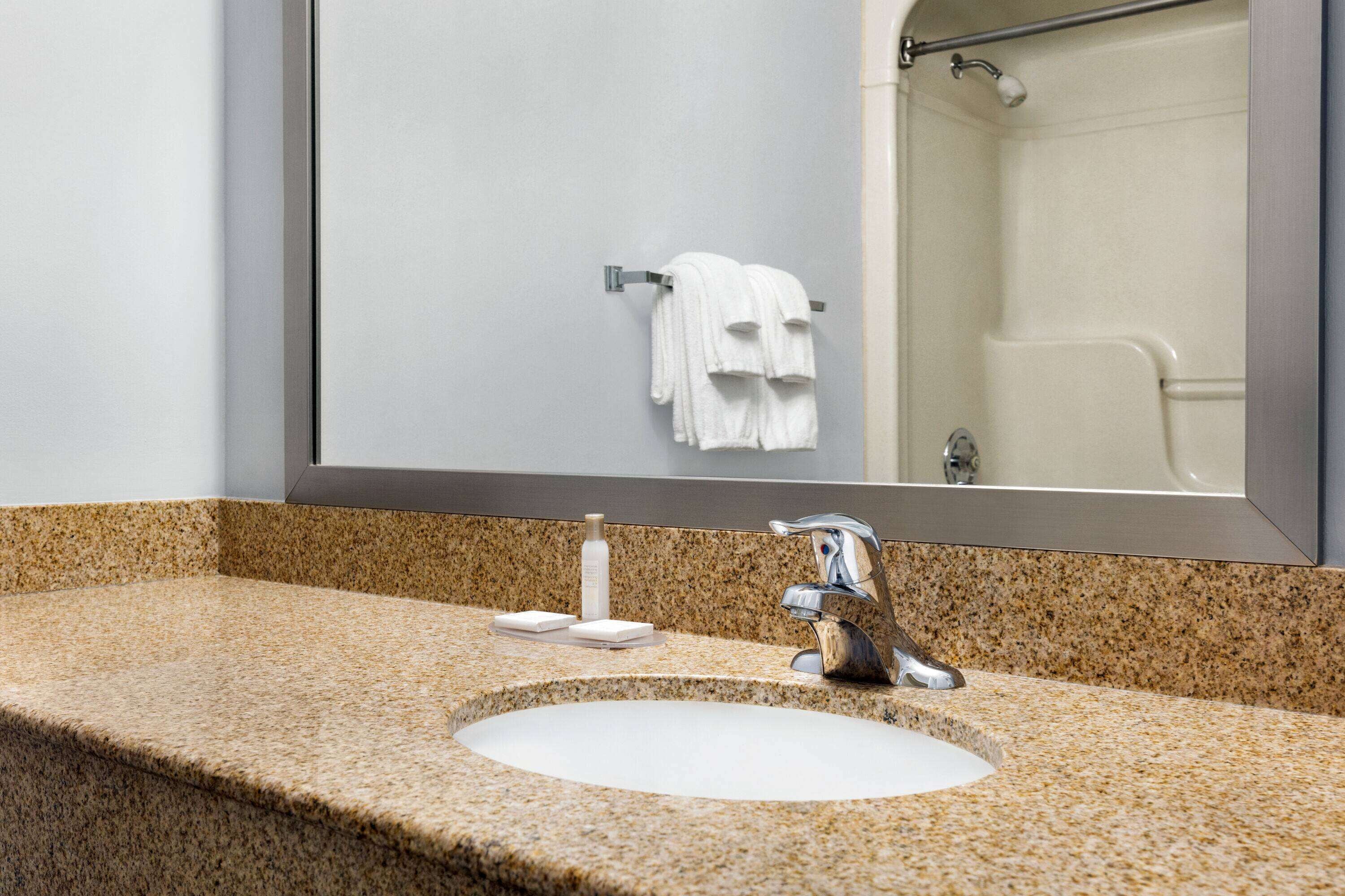 A bathroom with a granite countertop, a white sink, a mirror, and a towel rack with a white towel.