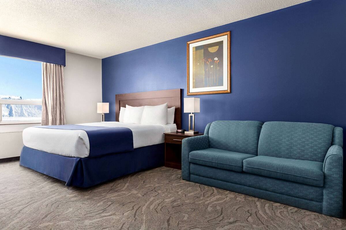 A hotel room with a bed, a sofa, a nightstand, a lamp, and a framed picture on the wall.