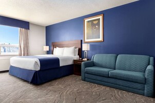 Habitación de hotel con una cama, un sofá, una mesita de noche, una lámpara y un cuadro en la pared.