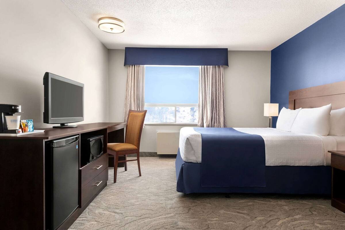 A hotel room with a bed, a desk with a television, a chair, and a window with curtains.