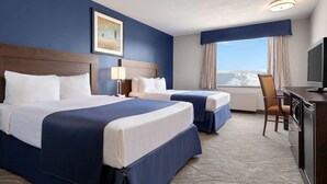 A hotel room with two beds, a desk with a television, a chair, and a large window with a view.