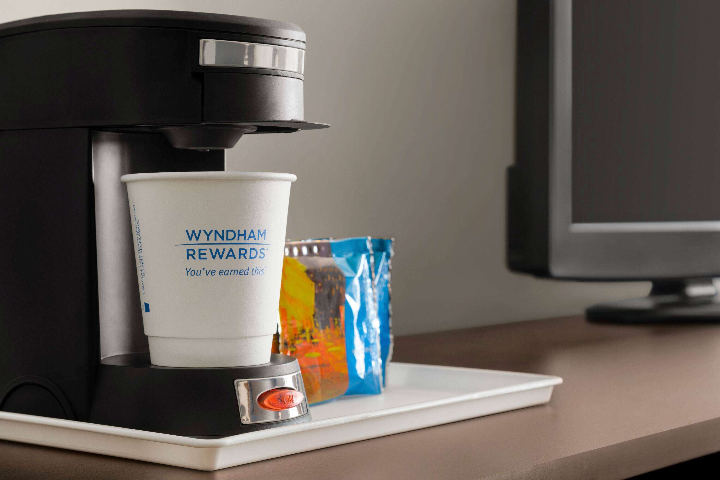 A coffee maker with a cup labeled "WYNDHAM REWARDS" and a colorful bag on a tray.