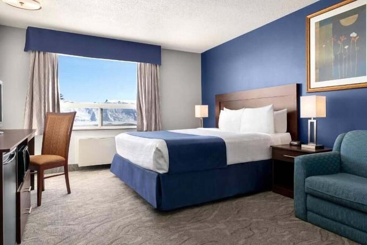 A hotel room with a bed, a desk, a chair, a couch, a painting, and a window with a view.