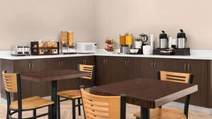 A modern kitchen with a dining area, equipped with a microwave, toaster, coffee maker, and various food containers.