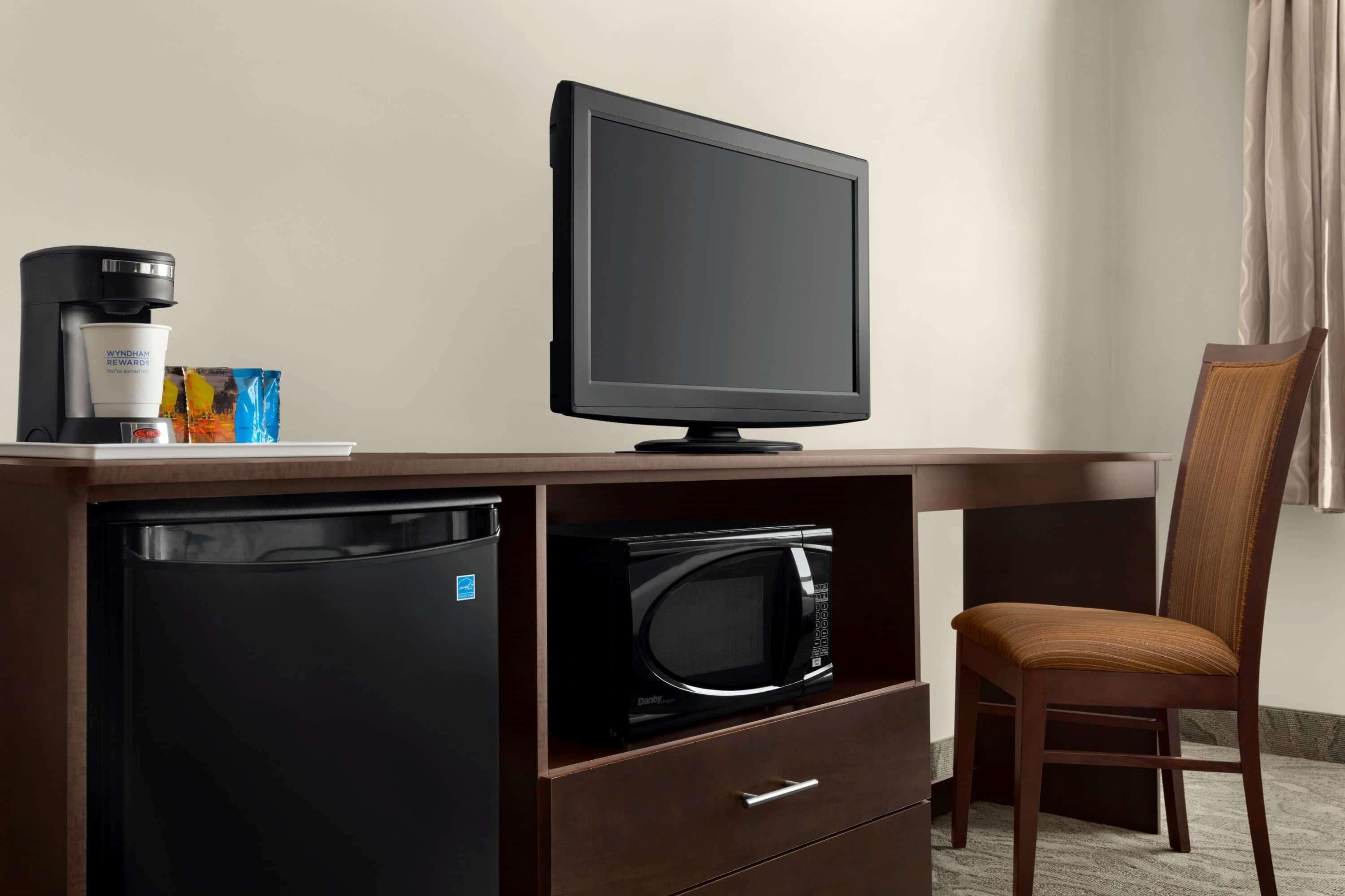 Habitación de hotel compacta con kitchenette, que incluye refrigerador, microondas, cafetera y televisión de pantalla plana.