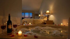 Una camera d'albergo con vasca, un letto, un comodino con una lampada e una bottiglia di vino.