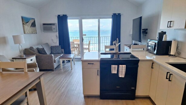 A modern kitchen with a stove, sink, and dining area. There is a balcony with a view of the sea. - Pointes North Beachfront Hotel – 2 Person Spa Tub Studios (Traverse City)