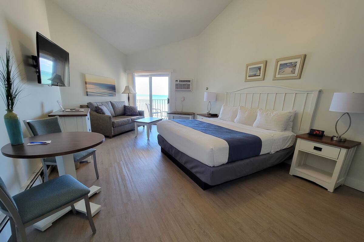 A hotel room with a bed, a desk, a chair, a sofa, a TV, and a window.