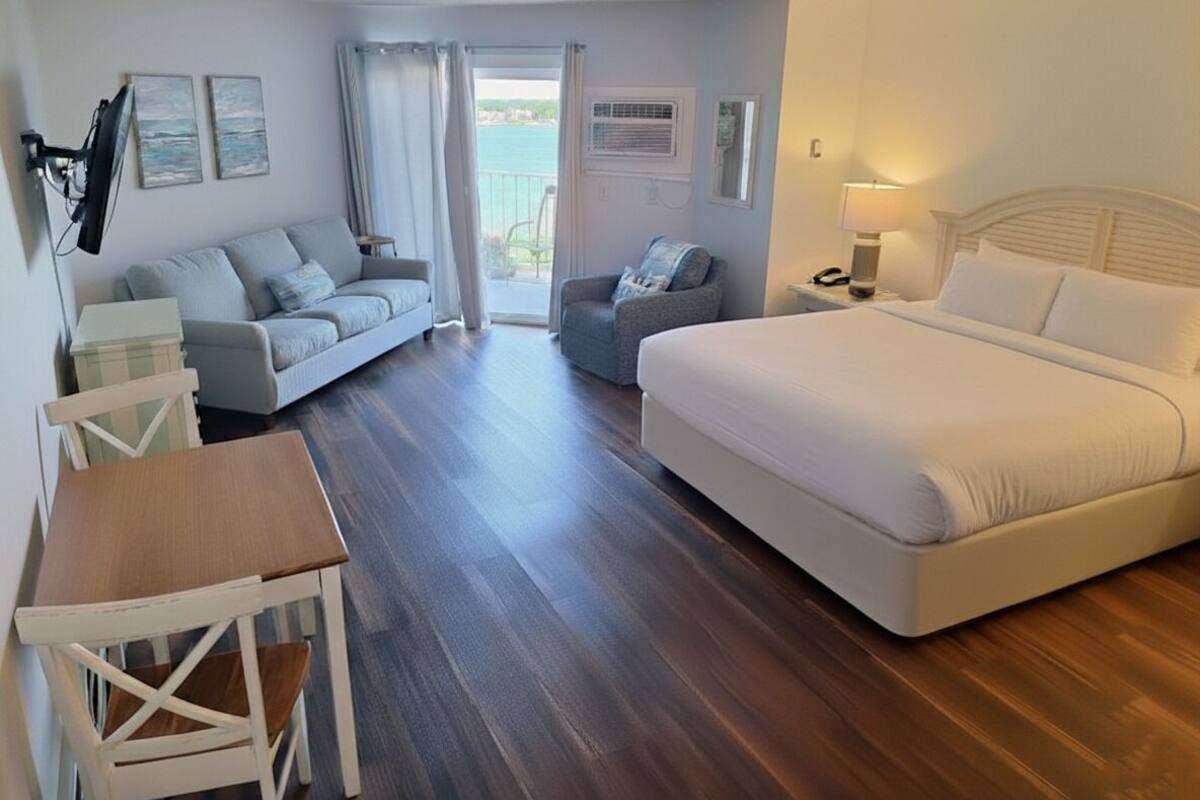 A hotel room with a bed, a sofa, a chair, a small table, and a view of the sea through a balcony.