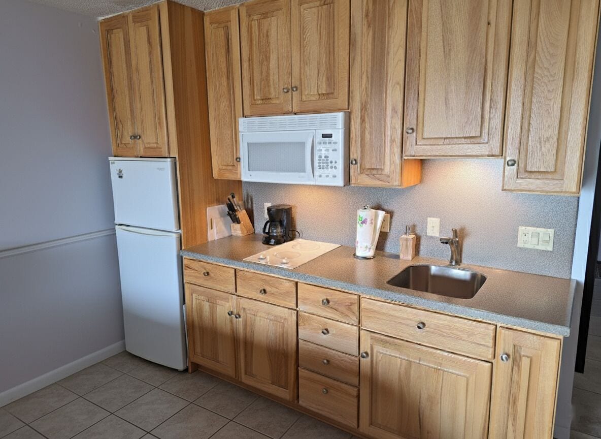 A kitchen with wooden cabinets, a white refrigerator, a microwave, a sink, and a countertop with various items.