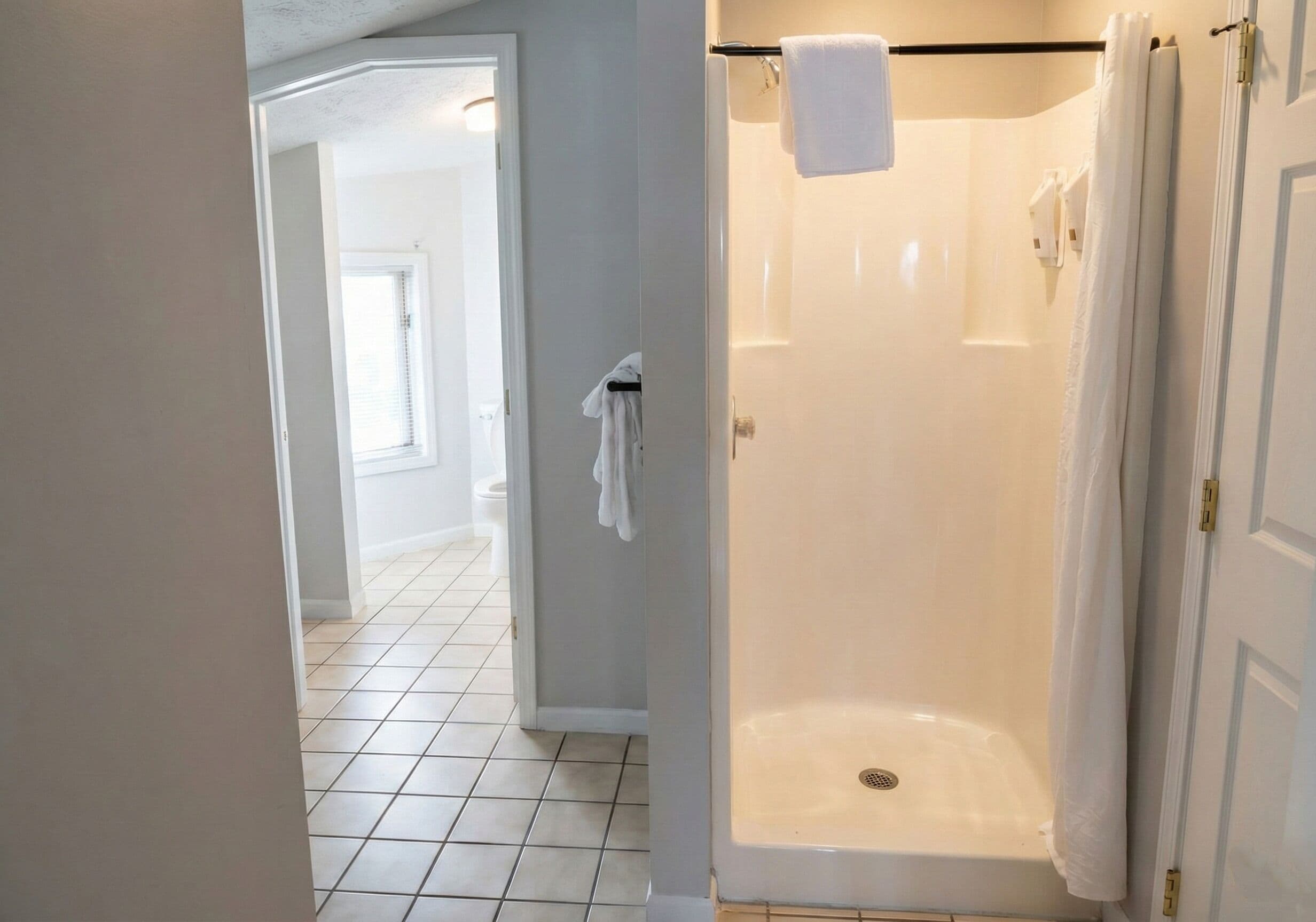 A walk-in shower with a white door, a towel hanging on the wall, and a tiled floor.