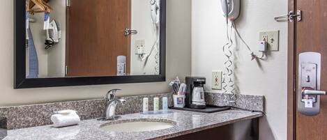 A bathroom with a granite countertop, a sink, a mirror, a hairdryer, and a coffee maker.