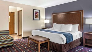 A hotel room with a large bed, a bench, a bedside table, and a wall-mounted lamp. - Comfort Inn Tulsa Midtown (Tulsa)