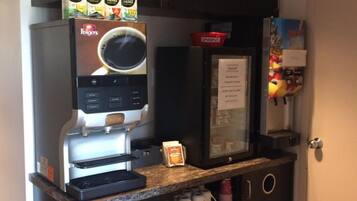 Una macchina del caffè con un espositore per tazze, un frigorifero con frutta in mostra e un forno a microonde.