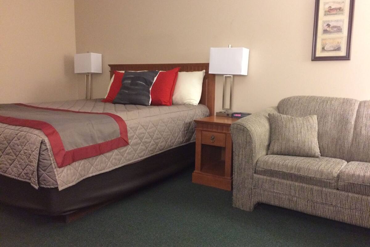 A hotel room with a bed, two bedside lamps, a nightstand, and a sofa.