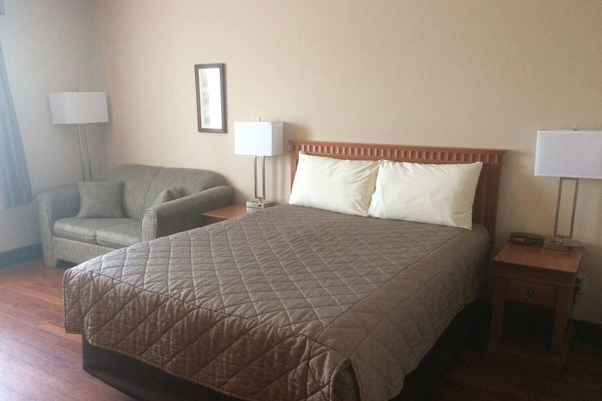 A hotel room with a large bed, a chair, two bedside tables, and a wall-mounted lamp.