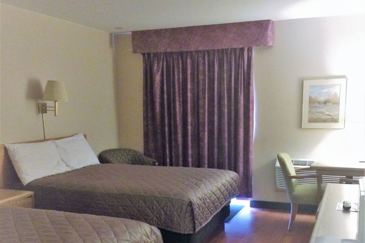 A hotel room with two beds, a desk, a chair, a lamp, and a painting on the wall.