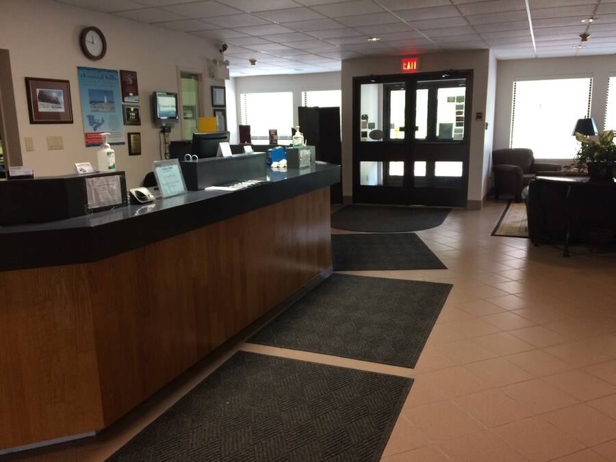 A reception area with a wooden reception desk, a clock, framed pictures, and a large window.