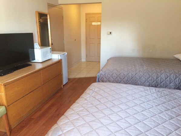 A bedroom with a wooden dresser, a television, a microwave, and two beds.