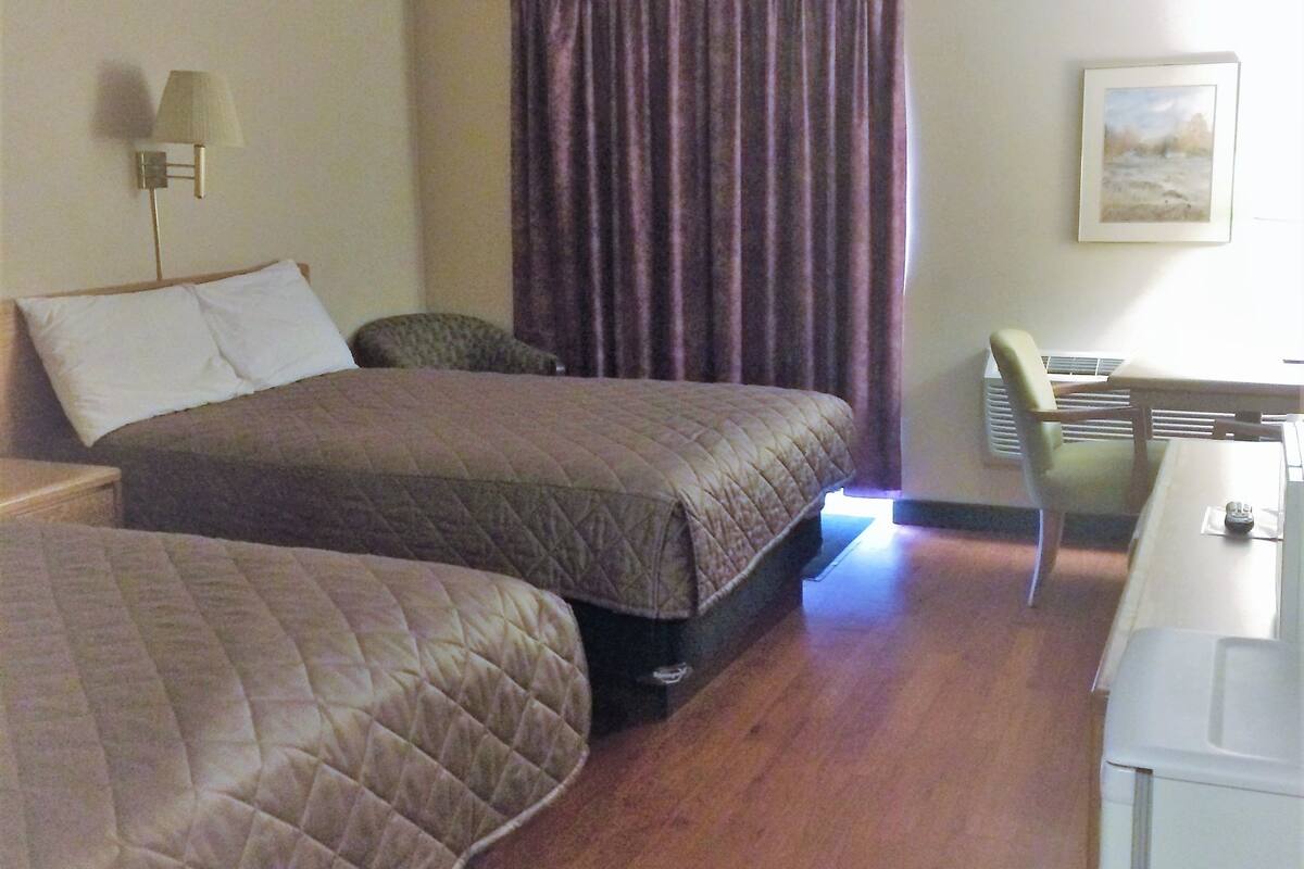 A hotel room with two beds, a desk, a chair, a lamp, and a window with curtains.