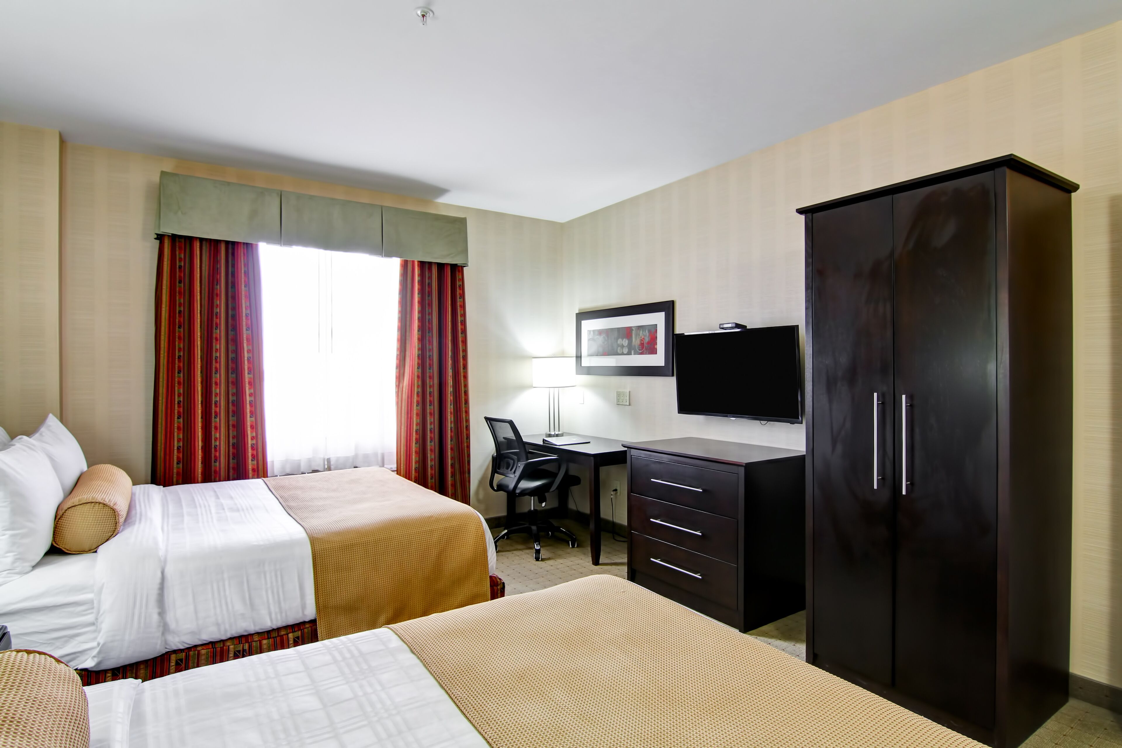 Una habitación de hotel con dos camas, un escritorio, una silla, un armario y un televisor.