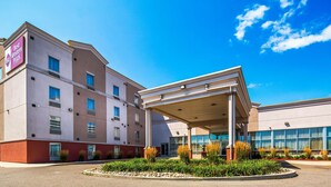 Un hotel con ingresso coperto, diverse finestre e un'area verde con piante.