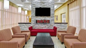 Una hall d'albergo con una parete in pietra, una TV a schermo piatto, un divano rosso, poltrone a righe e un tavolino da caffè.