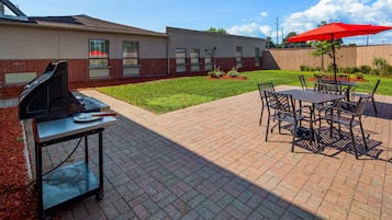 Zona de terrassa amb una barbacoa, taula i cadires d'exterior i un parasol vermell.