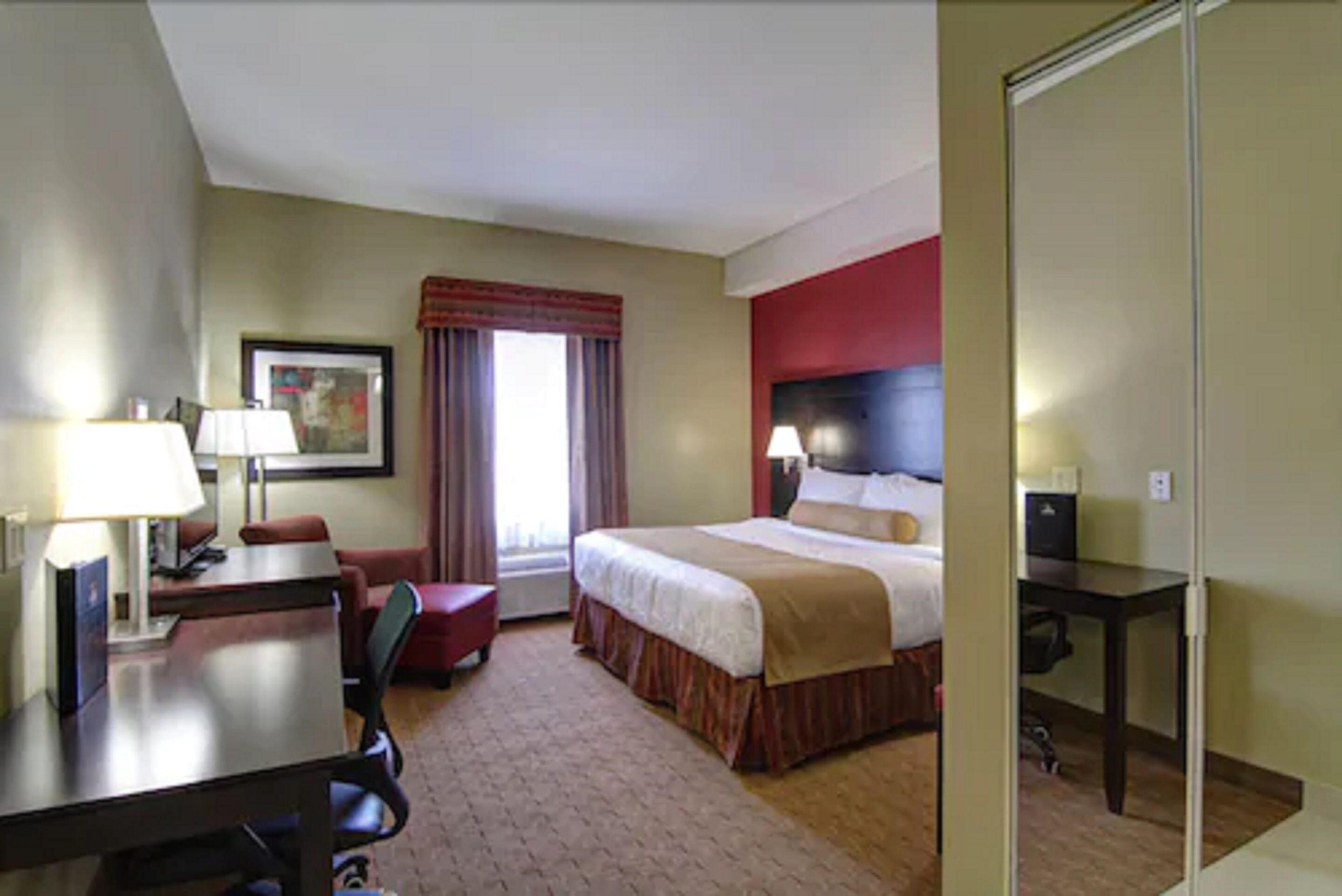 A hotel room with a bed, desk, chair, and a window with curtains.